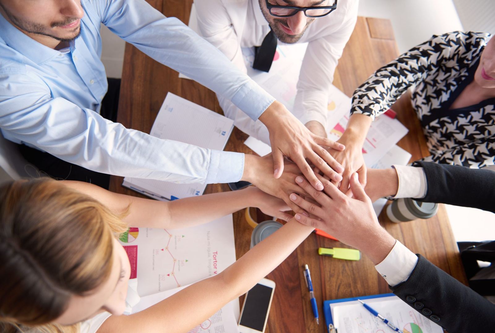 Equipo de trabajo uniendo sus manos sobre una mesa de juntas